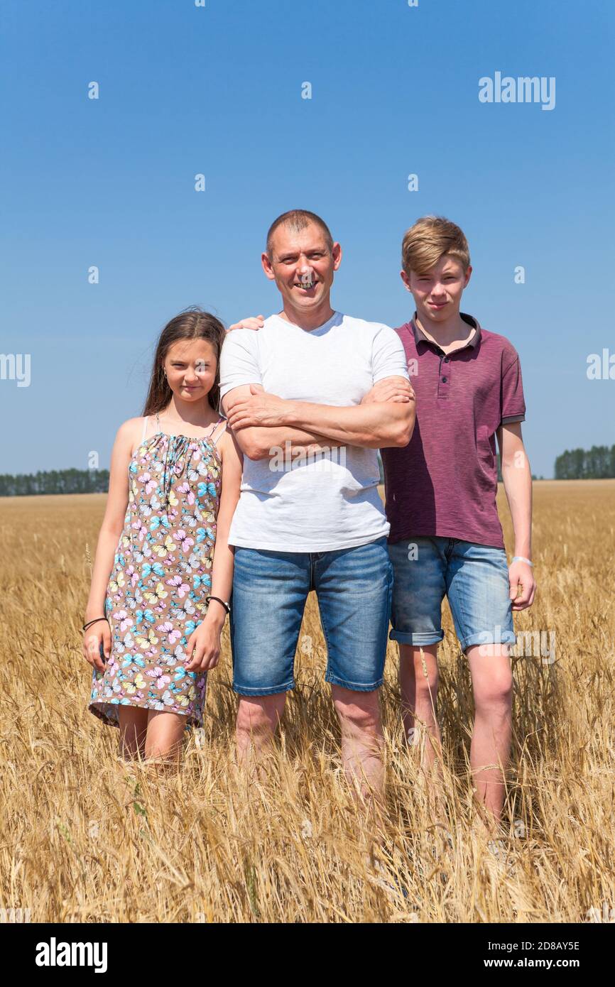 Vater mit Sohn und Tochter, Porträt in voller Länge, alleinerziehender Vater mit zwei Kindern, die im Sommer auf dem Weizenfeld stehen Stockfoto