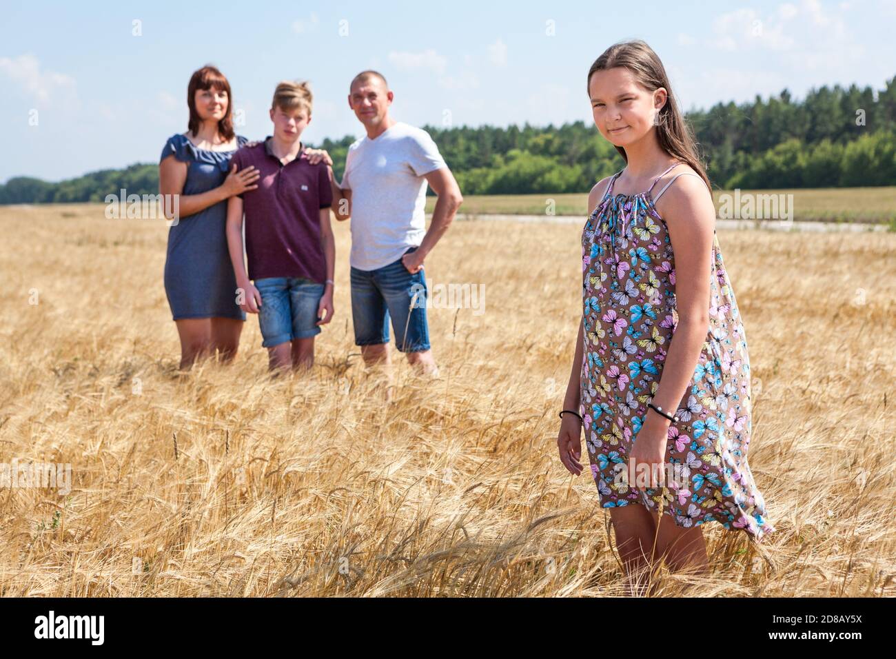 Konzept eines Adoptivkindes, junges Mädchen im Vordergrund mit Adoptivfamilie im Hintergrund, Stieftochter mit Vater, Mutter und Bruder Stockfoto