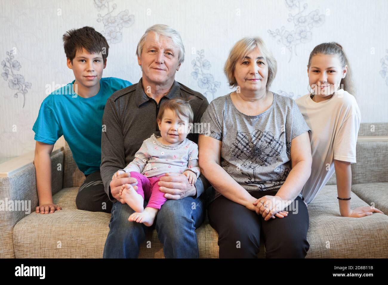 Seniorenpaar mit Enkelkindern im Teenageralter und Kleinkind-Enkelportrait, sitzend auf einer Couch zu Hause Stockfoto