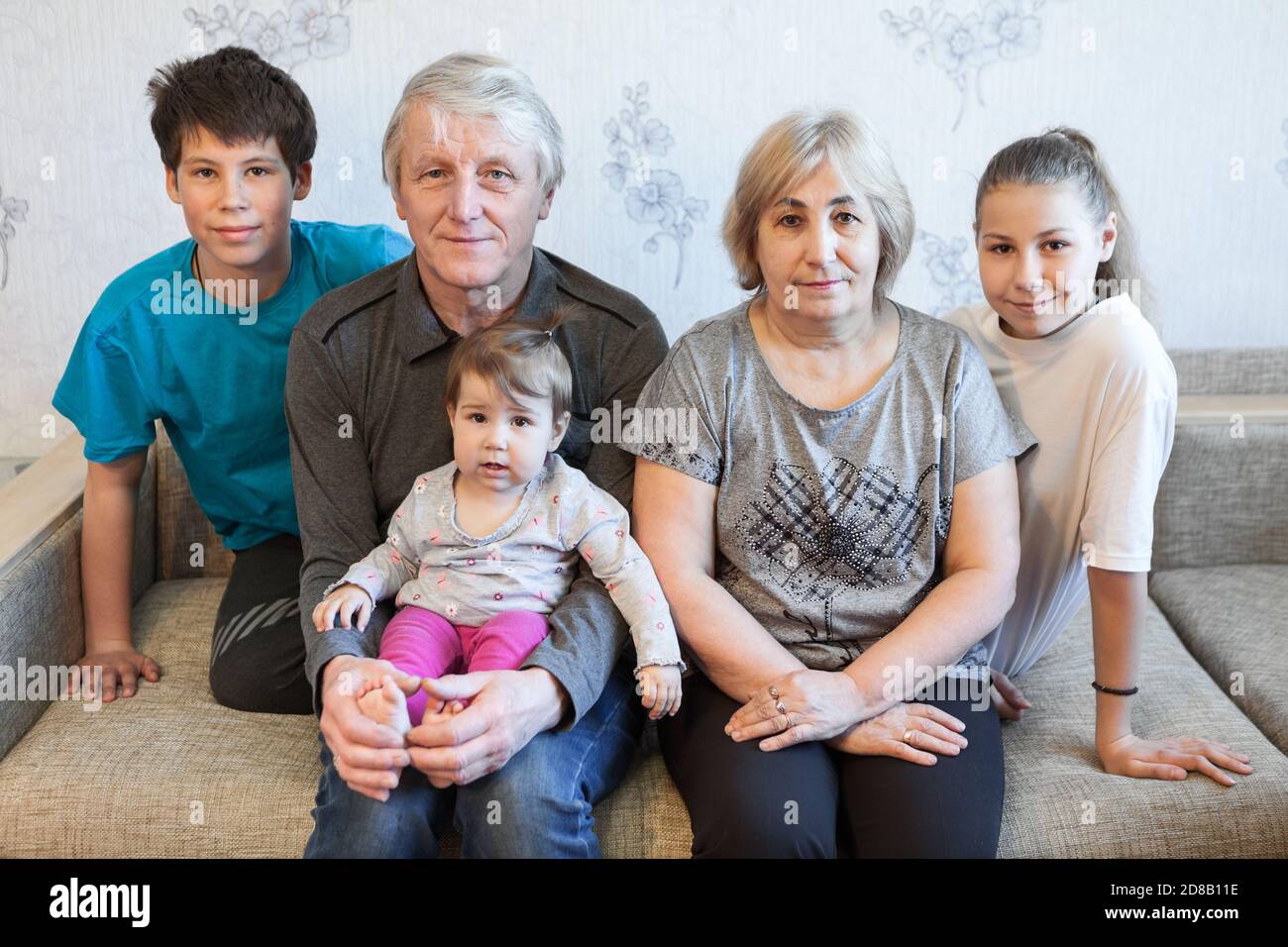 Kaukasische Familie mit Kindern im Teenageralter, Kleinkind und älteren Eltern, die zu Hause auf dem Sofa sitzen. Glückliches und entspannendes Familienportrait Stockfoto