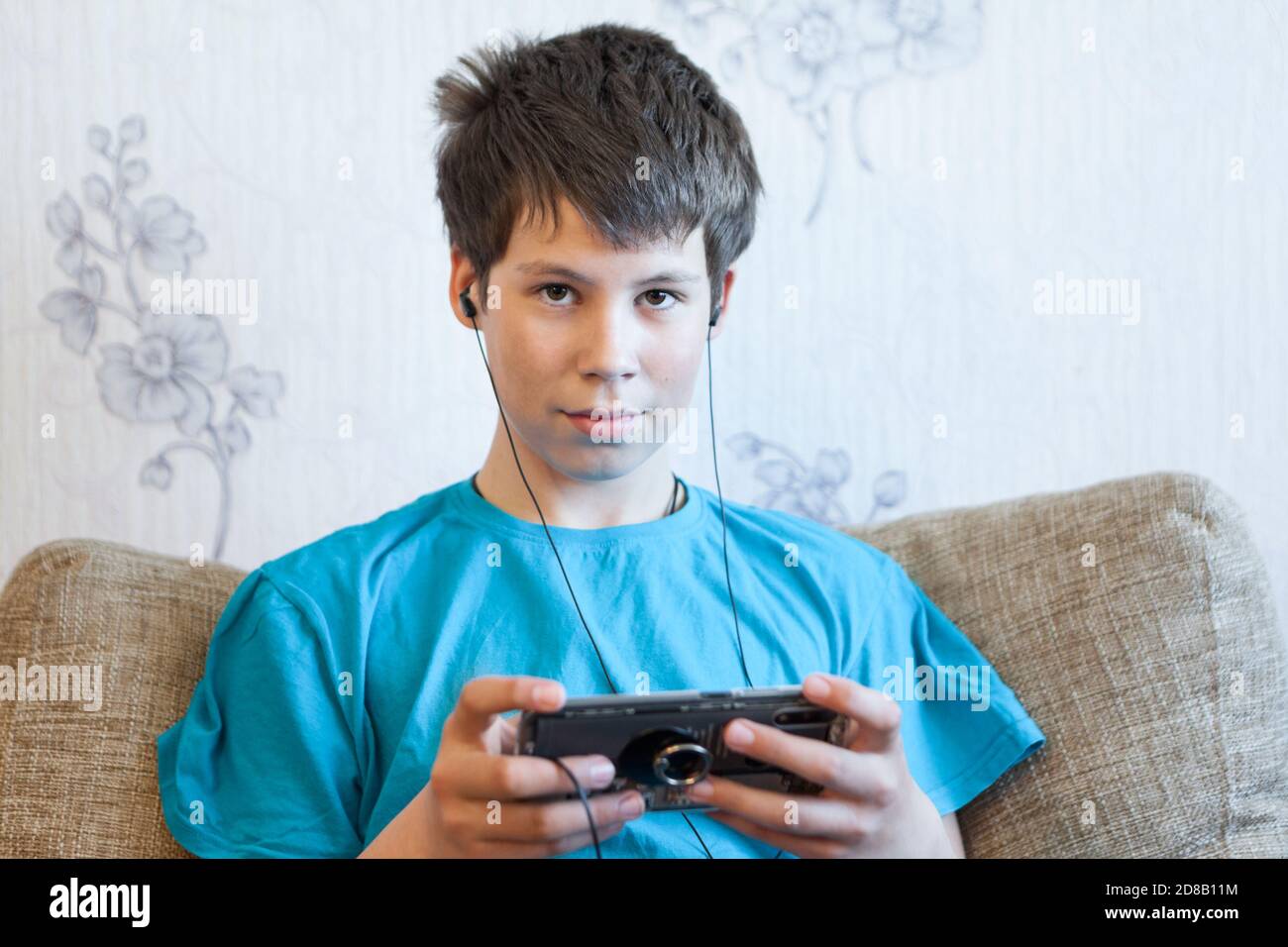 Kaukasischer Teenager Junge mit seinem Handy in Innenräumen, die Musik hören und Blick auf die Kamera Stockfoto