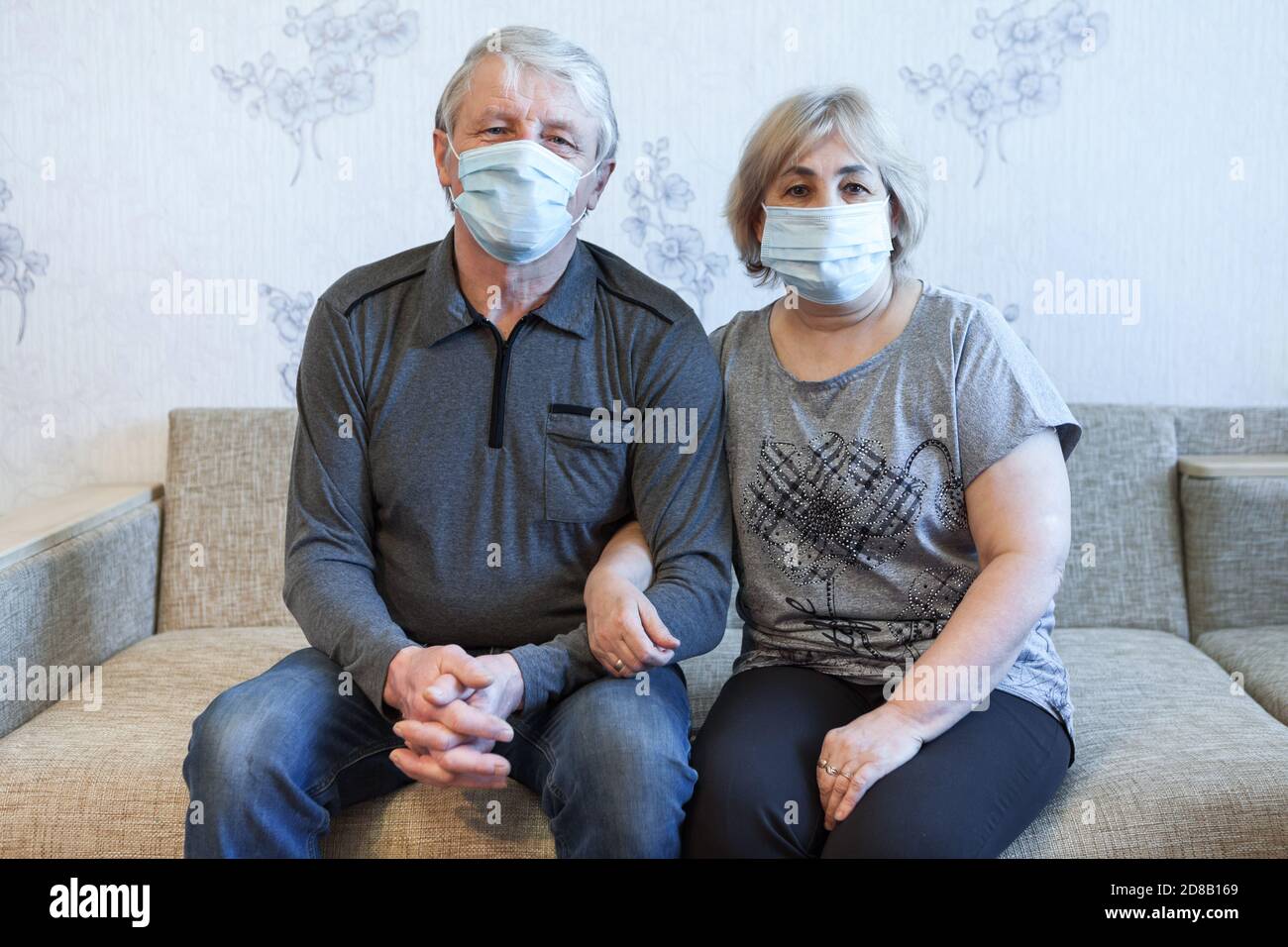 Ältere kaukasische Paar sitzt auf einer Couch zu Hause, zwei Personen tragen medizinische Masken Stockfoto