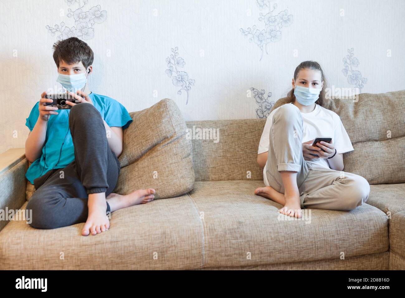 Porträt von zwei Jugendlichen Kinder sitzen in der Ferne auf einer Couch zu Hause, halten Handys Stockfoto