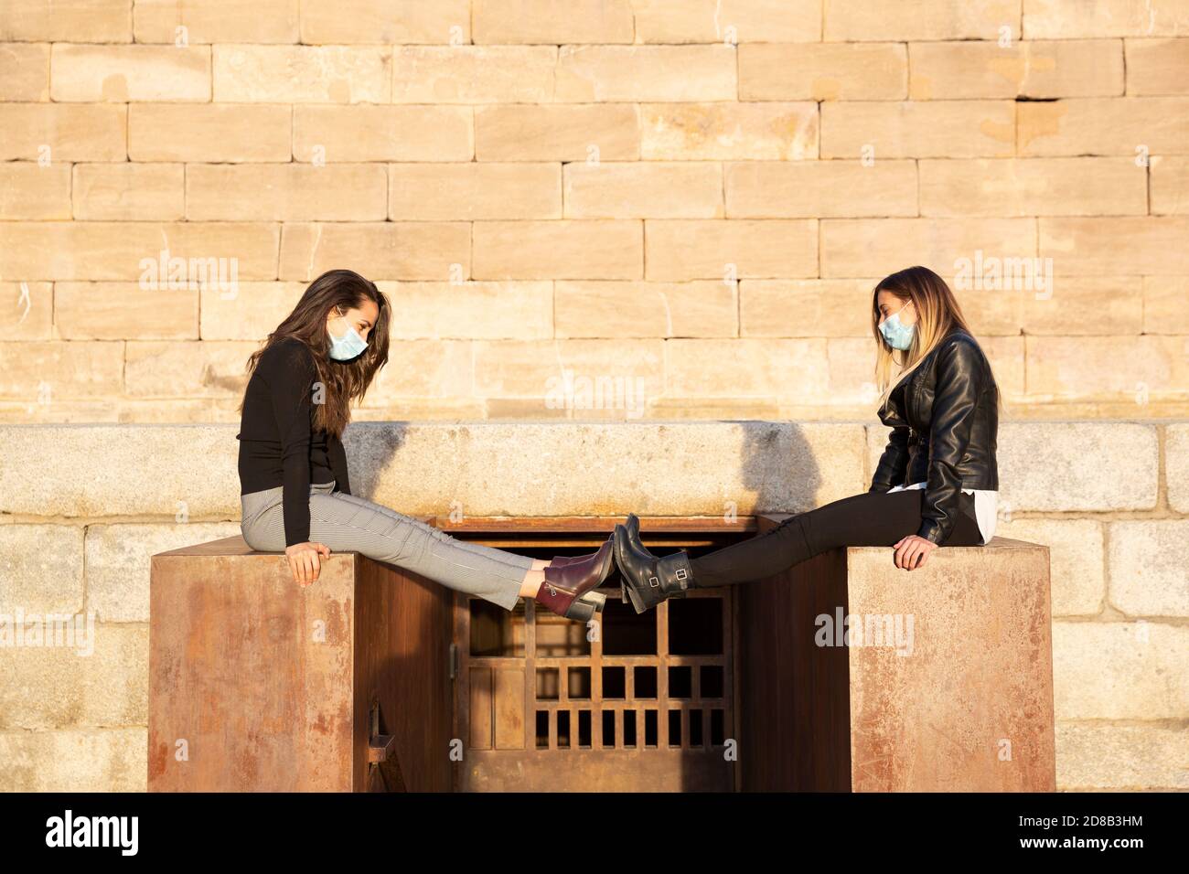 Zwei Mädchen mit einer Gesichtsmaske halten soziale Distanz durch die Verlängerung ihrer Beine. Sie sind im Freien. Stockfoto
