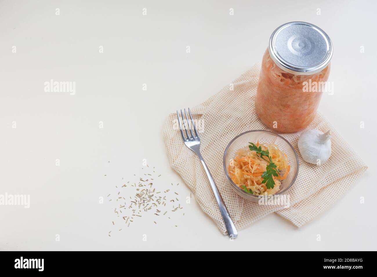 Ein Glas mit fermentiertem Kohl, etwas Salat auf dem Teller und Gewürzen auf hellem Hintergrund Stockfoto