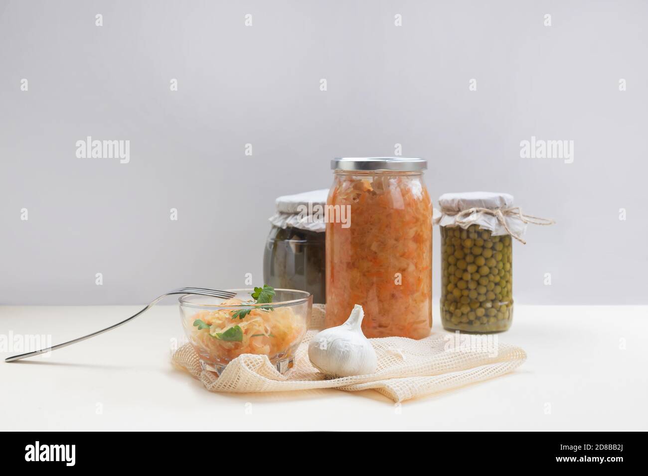 Hausgemachte Gläser mit fermentiertem Kohl, Erbsen, eingelegten Gurken auf hellem Hintergrund, etwas Sauerkraut in einer Glasschüssel Stockfoto