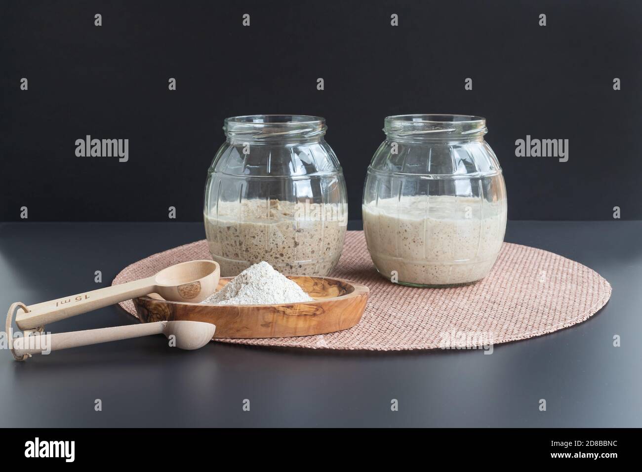 Natürliche Bio-Sauerteig-Vorspeisen: Frisch fermentierte Roggen- und Weizenvorspeisen in Gläsern, die zur Herstellung von Sauerteig-Brot verwendet werden können Stockfoto