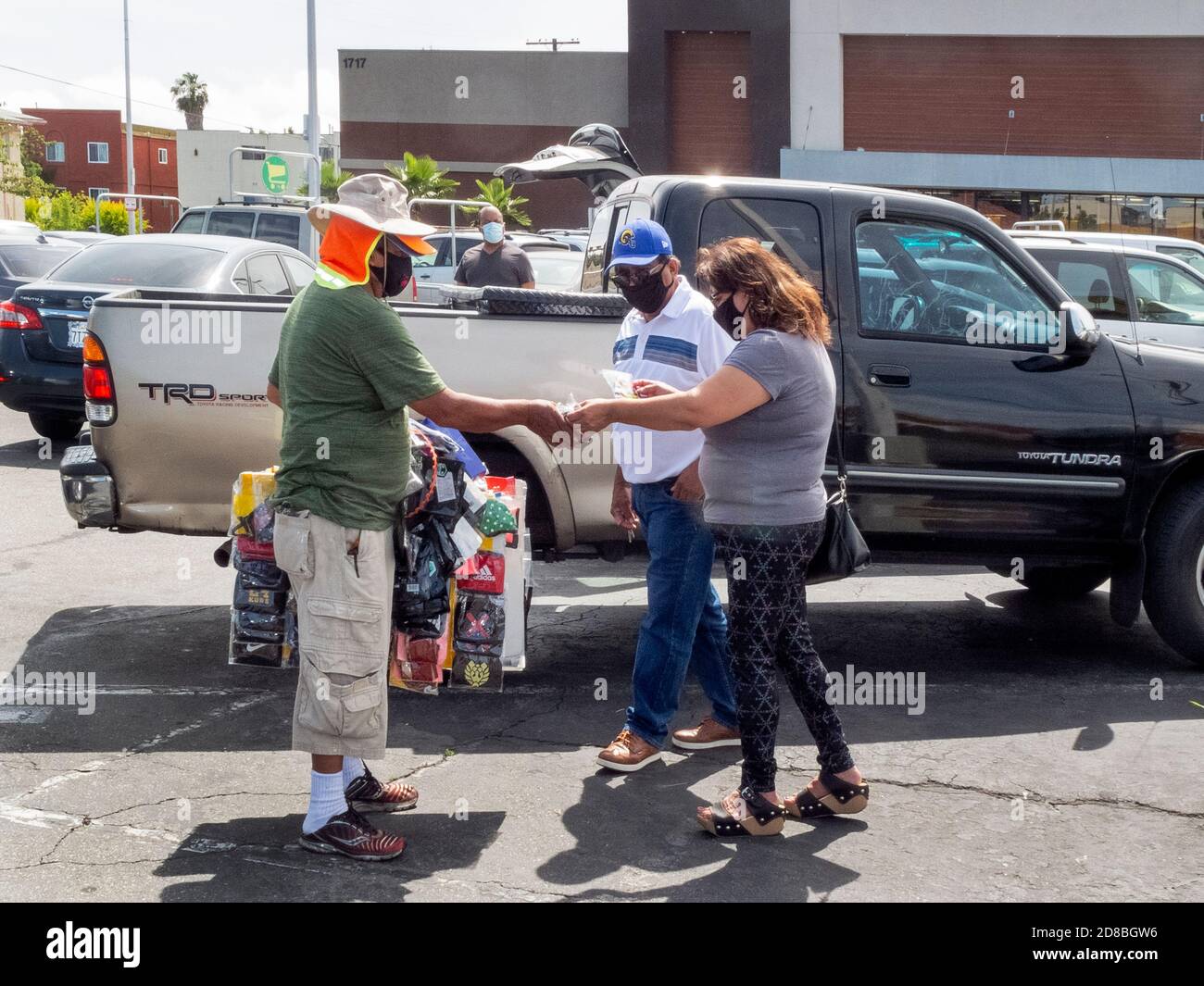 Ein hispanischer Verkäufer trägt ein tragbares Display mit farbenfrohem Gesicht Masken während der Coronavirus Pandemie als Paar macht ein Kauf in einem Los Angeles pa Stockfoto