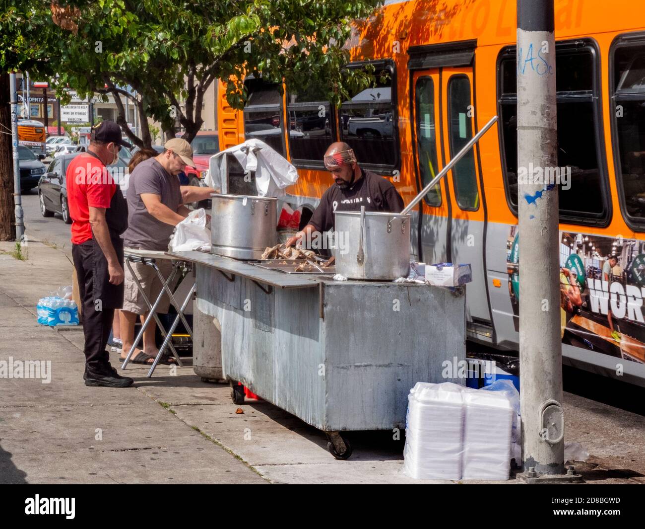 Mit Restaurants geschlossen in der Coronavirus Pandemie, ein unternehmungslustiger hispanischer Koch bewegt seinen Grill und Töpfe im Freien auf den Bürgersteig an einer Bushaltestelle in Stockfoto