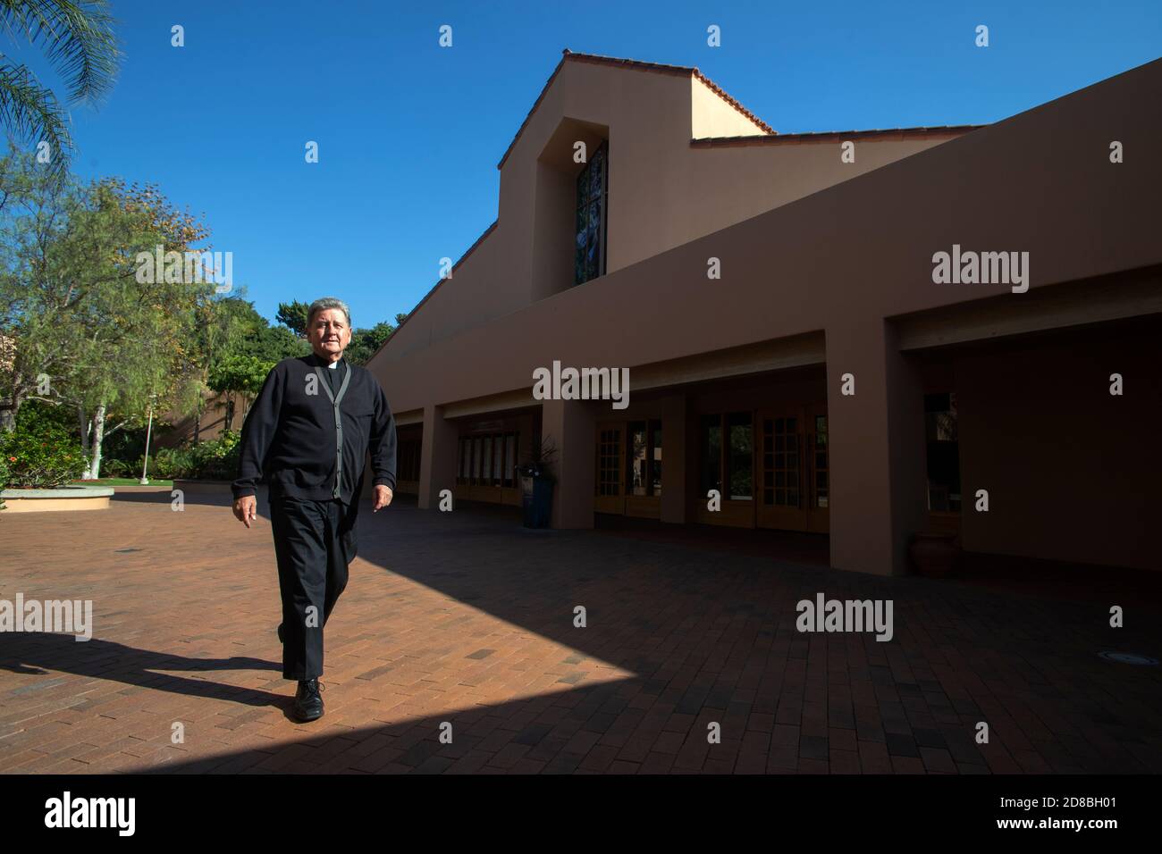 Der monsignore einer katholischen Kirche in Südkalifornien geht über den Kirchenhof nach Sonne und Schatten. Stockfoto