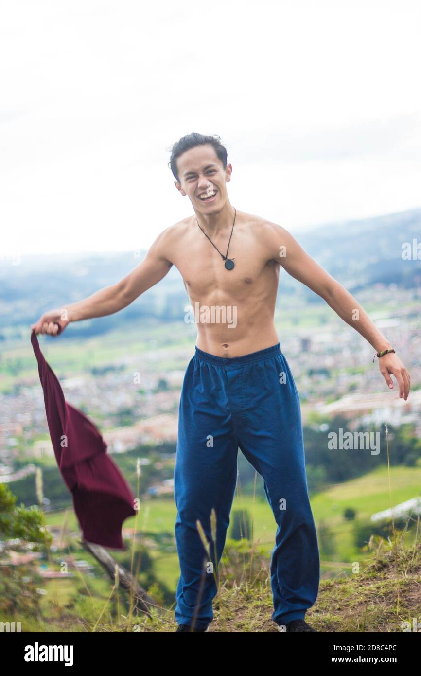 Flacher Fokus eines lächelnden jungen Mannes, der ein abzieht t-Shirt auf einem Hügel Stockfoto
