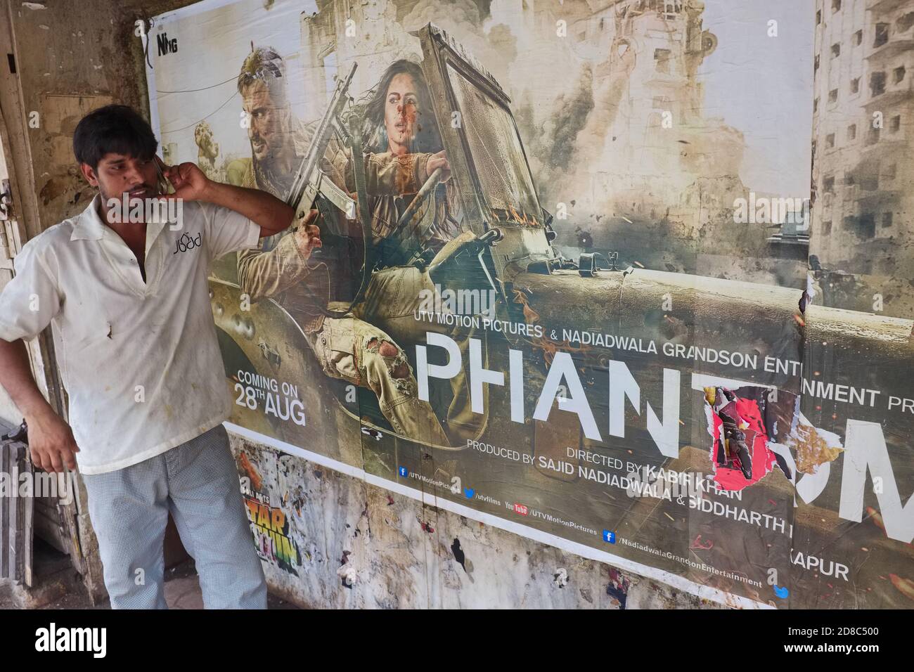 Vor einem Arbeiterkino in Pathe Bapurao Marg, Mumbai, Indien, spricht ein Mann auf seinem Handy vor einem Plakat des Hindi-Sprachfilms 'Phantom' Stockfoto