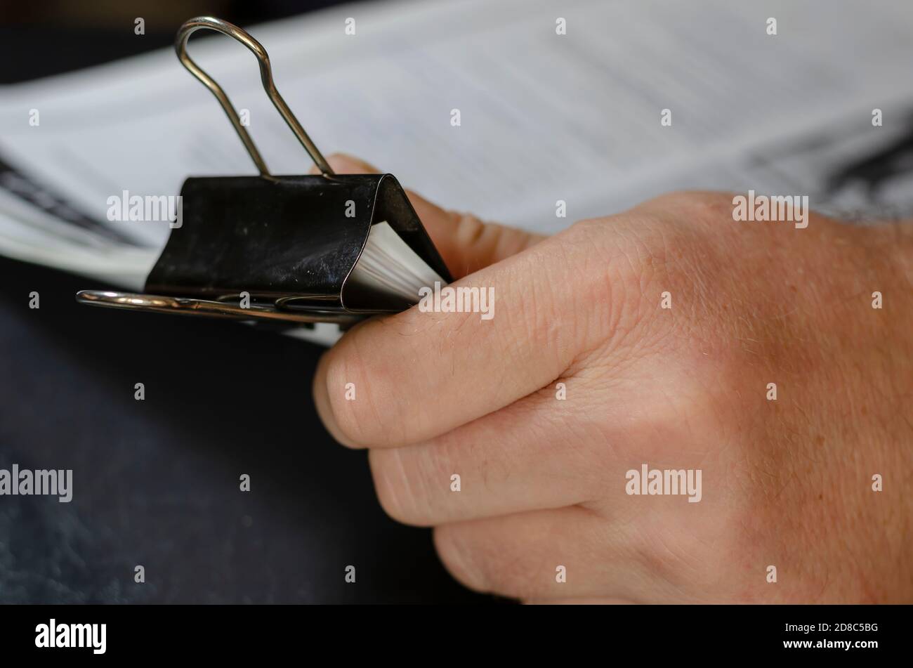 Nahaufnahme von männlichen Händen, die Papierblätter mit schwarzer Metallklammer halten. Die Blätter sind mit Text gefüllt. Spuren von blauer Tinte auf dem Finger des Menschen. Selektiver Fokus. Stockfoto