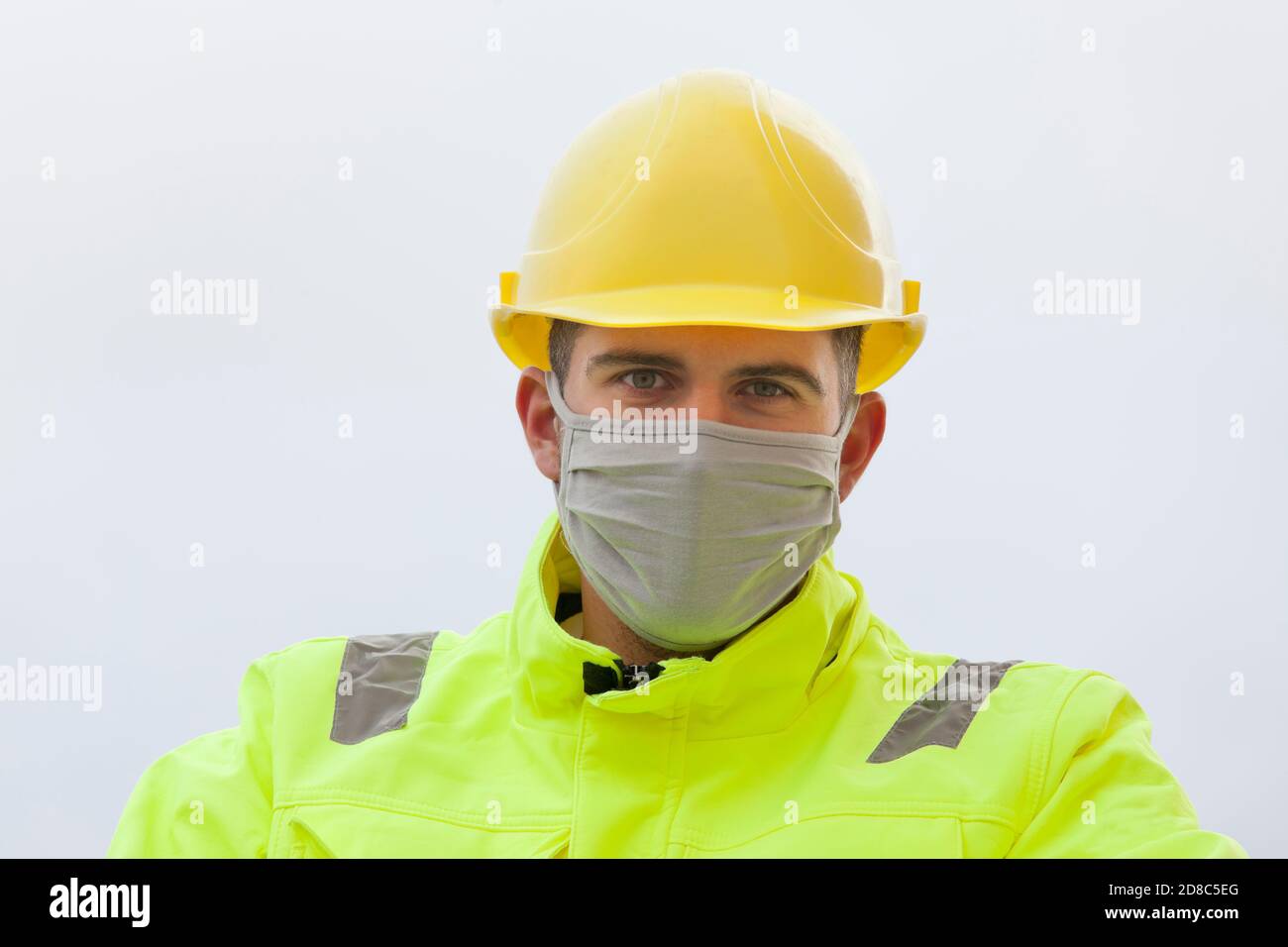 Portrait von lächelnden jungen Ingenieur mit Gesichtsmaske und hart mütze und Arbeitsschutzkleidung Stockfoto