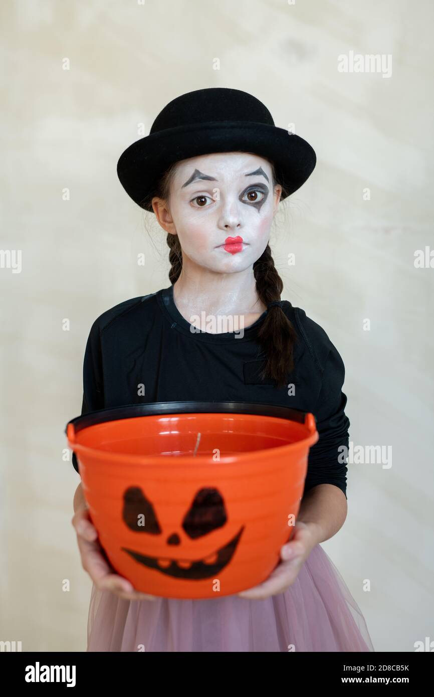 Portrait von schweren schockiert Pantomime Mädchen in schwarzem Hut hält orange behandeln Eimer mit unheimlich Gesicht Bild vor isoliertem Hintergrund, Halloween-Konzept Stockfoto