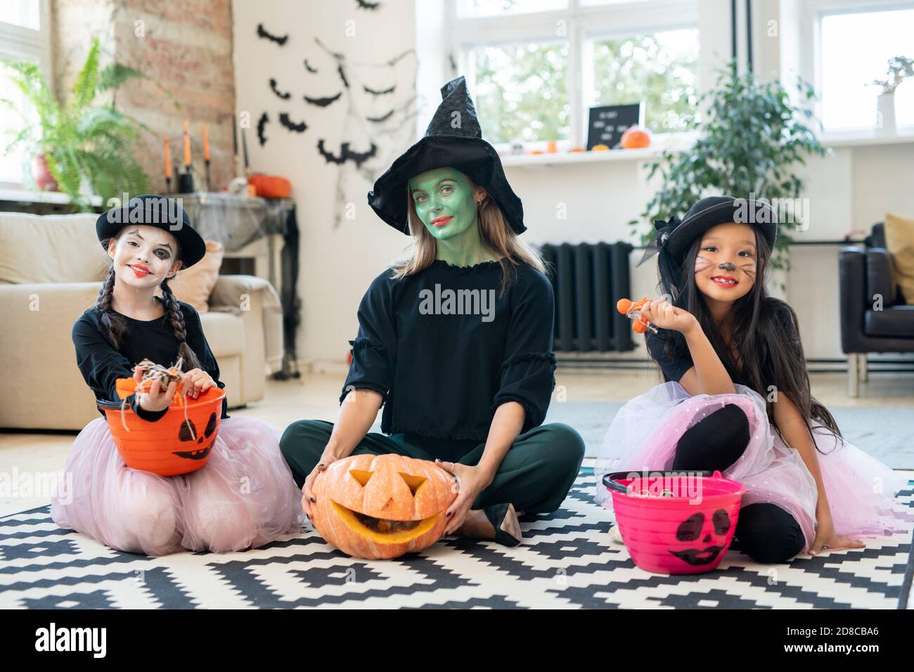 Drei hübsche Hexen sitzen mit Trick-or-treating Eimer auf dem Boden und Blick auf die Kamera, während genießen Halloween-Party Stockfoto