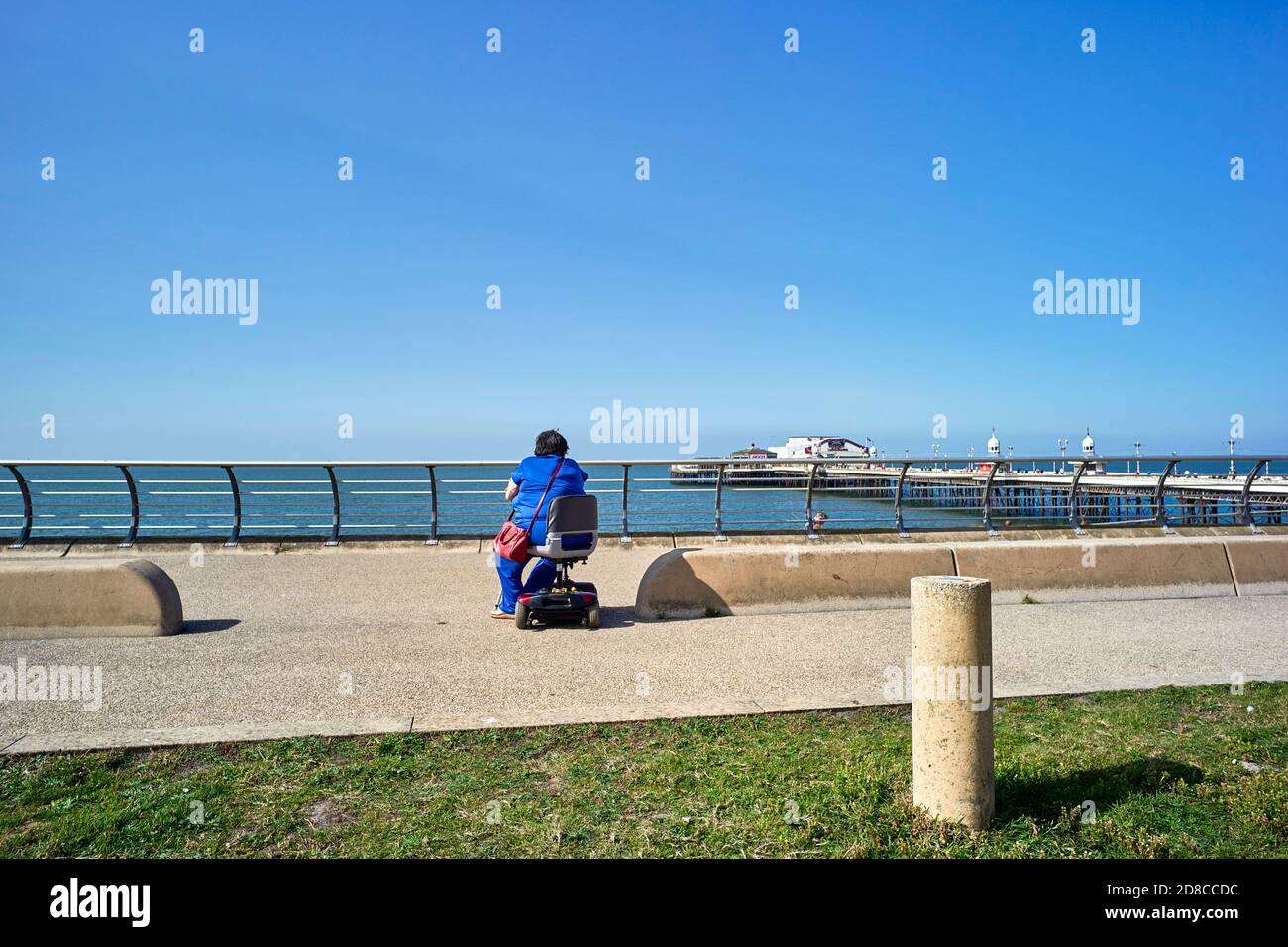 Ältere Frau auf eigene Faust auf einem Mobilitätsroller sitzen Blick auf das Meer bei Blackpool Stockfoto