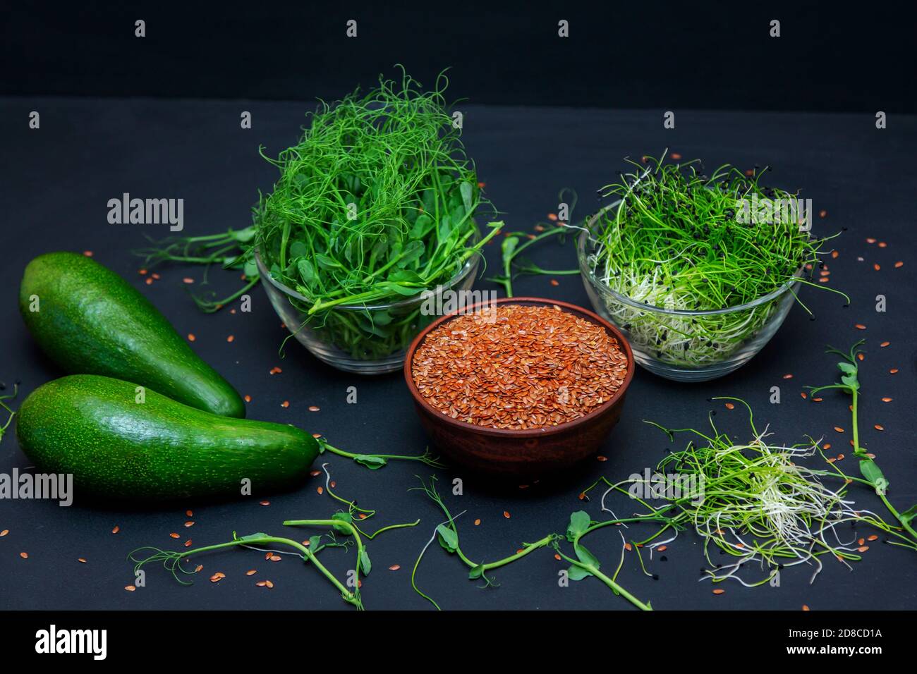 Microgreens: Grüne Erbsen und Zwiebelsprossen, Leinsamen in Glasschüsseln und Avocado auf schwarzem Hintergrund. Gesunde vegetarische Ernährung und Diät-Konzept. Stockfoto
