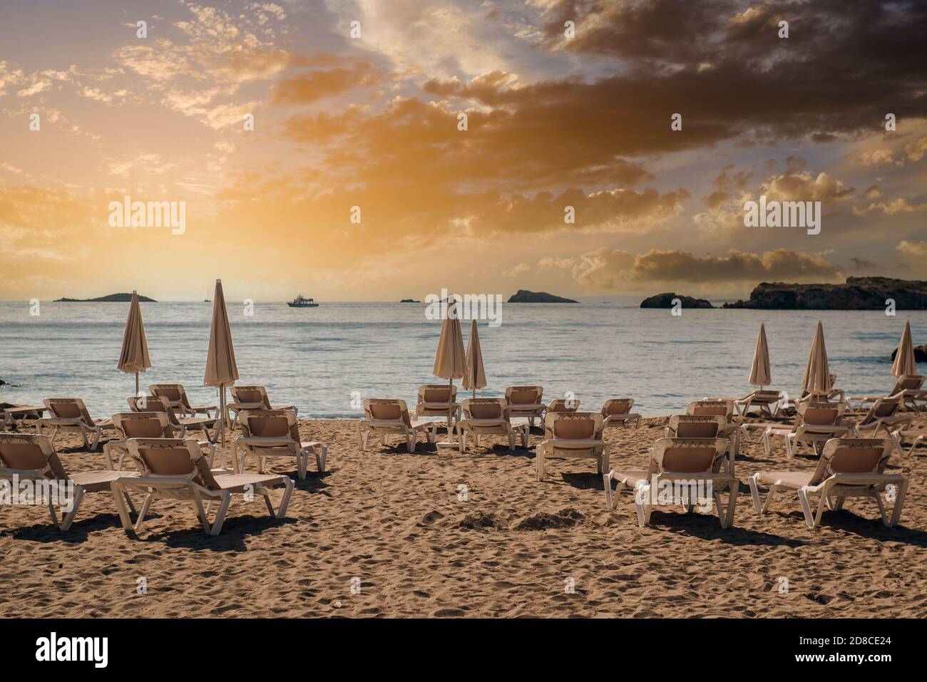 Sonnenschirme und Liegestühle am Strand von Ibiza Resort auf bewölktem Himmel Hintergrund, malerischen Sonnenuntergang glühende Sonne Panoramablick Balearen. Spanien Stockfoto