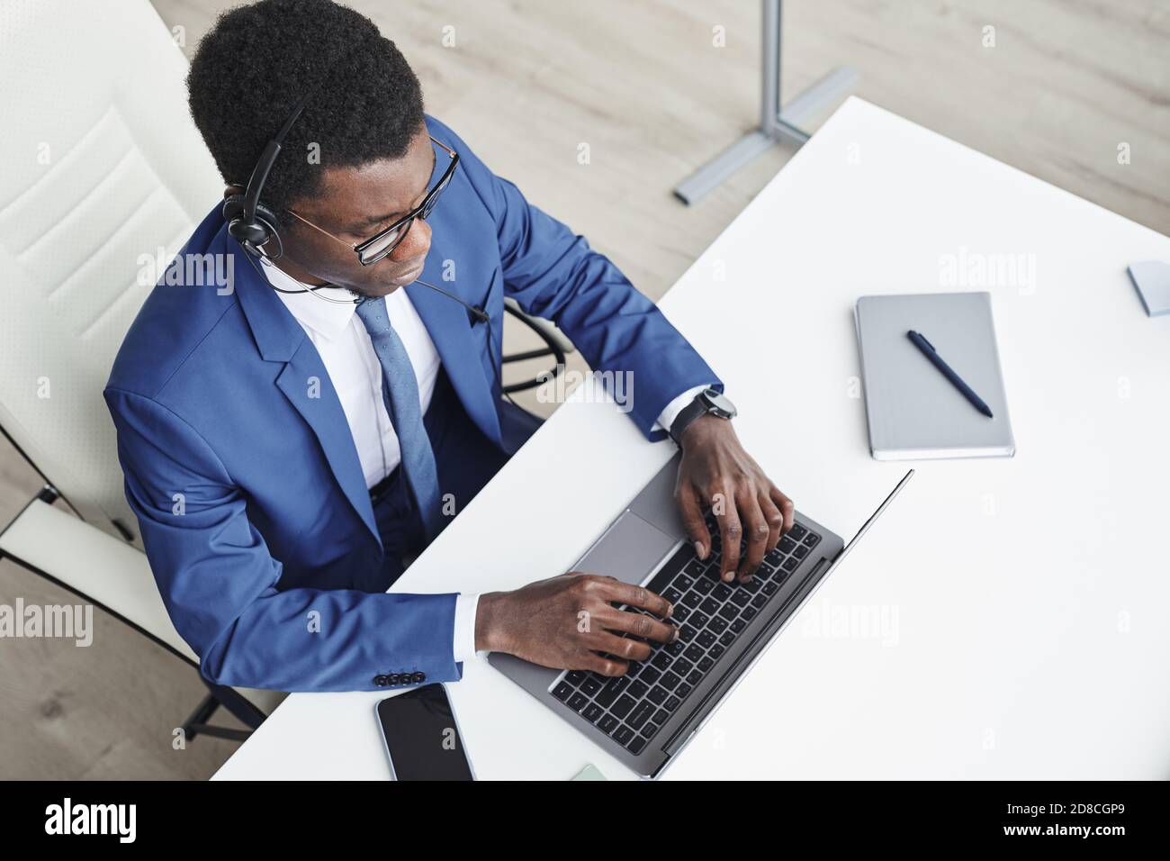 High-Angle-Ansicht der afrikanischen Geschäftsmann in Kopfhörer tippen auf Laptop und Online-Kommunikation an seinem Arbeitsplatz im Büro Stockfoto