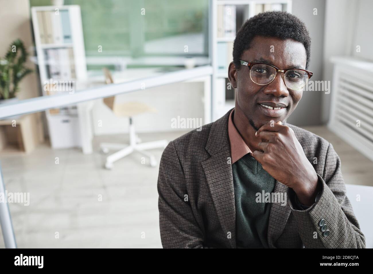 Portrait von afrikanischem jungen Büroangestellter im Anzug lächelnd Kamera während der Arbeit im Büro Stockfoto