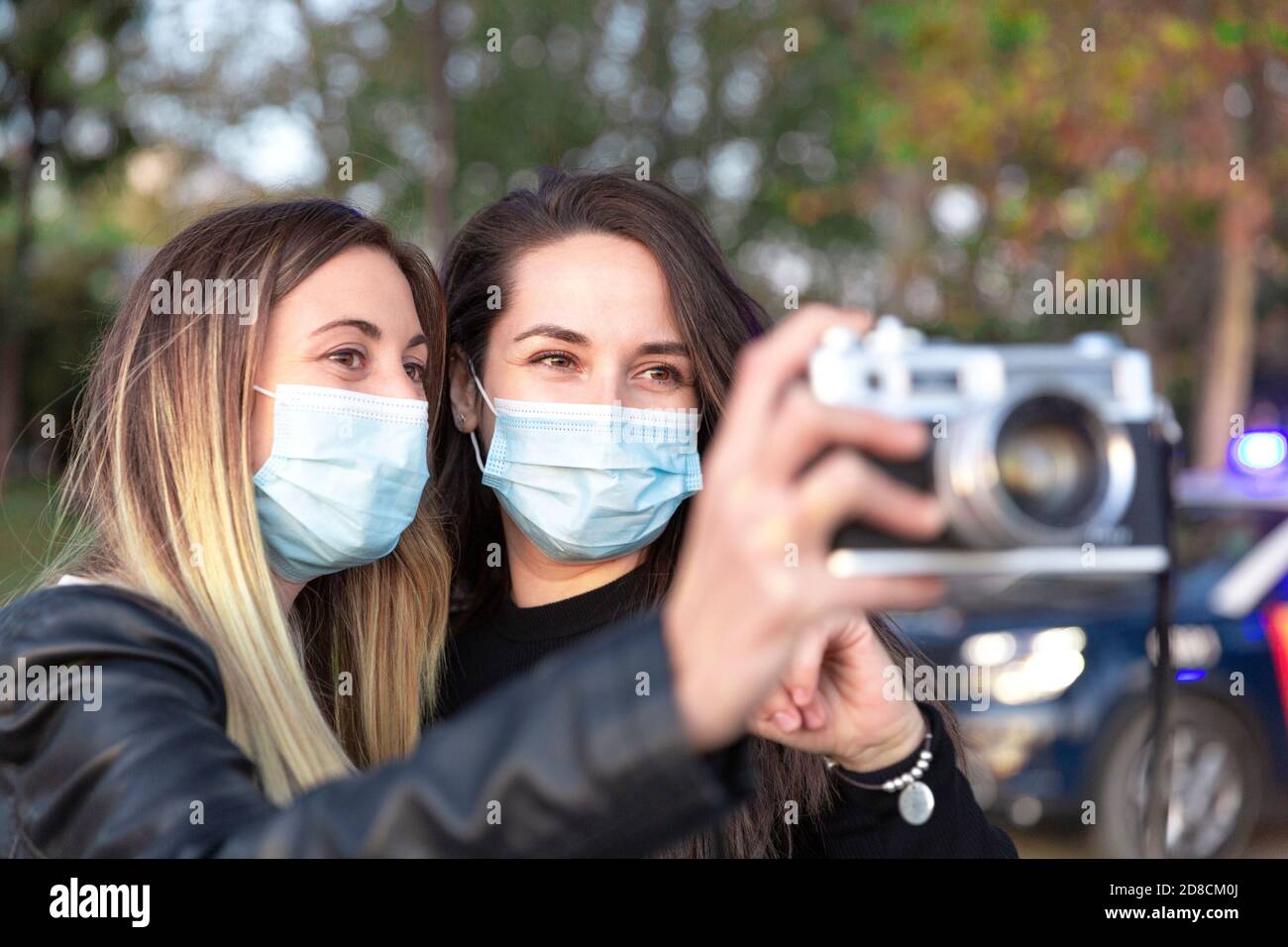 Nahaufnahme von zwei Mädchen, die Gesichtsmasken mit einer analogen Kamera in den Händen tragen. Stockfoto
