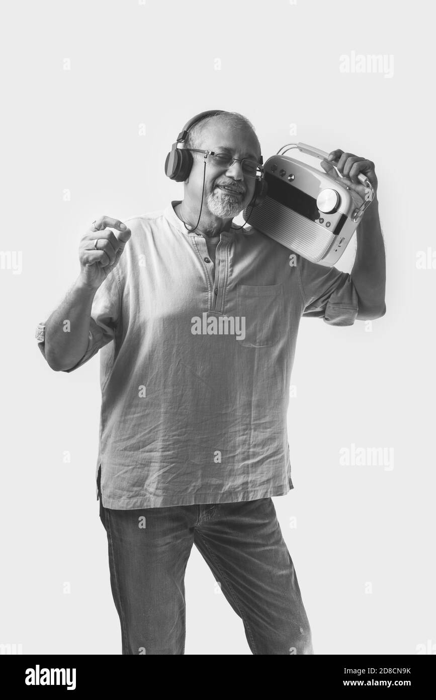 Indischer asiatischer alter Mann oder männlicher älterer Erwachsener, der Musik im Vintage-Radio mit Kopfhörern hört und vor weißem Hintergrund tanzt Stockfoto