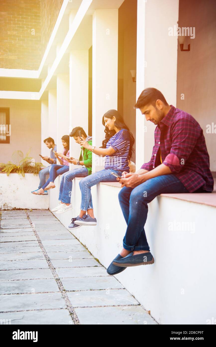 Asiatische indische College-Studenten mit Smartphone, während im College-Campus sitzen, cel Telefon sucht Stockfoto