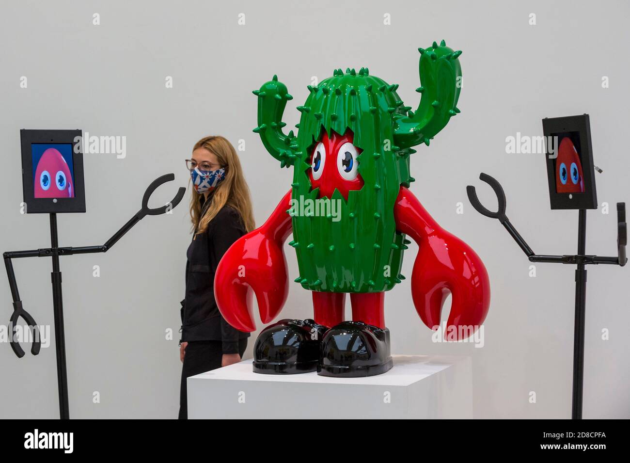 London, Großbritannien. 29. Oktober 2020. Ein Mitarbeiter posiert mit einem Kaktuskunstwerk und einem Roboter zum Betrachten. Vorschau auf „Philip Colbert: Lobsteropolis“, eine neue Ausstellung in der Saatchi Gallery am Sloane Square. Die neue Ausstellung Lockdown Inspired ist per Roboter ferngesteuert zu sehen. Die Ausstellung (29. Oktober – 29. November) ist die bisher größte britische Übersicht über Colberts Universum und umfasst unsichtbare großformatige Gemälde und Skulpturen. Kredit: Stephen Chung / Alamy Live Nachrichten Stockfoto