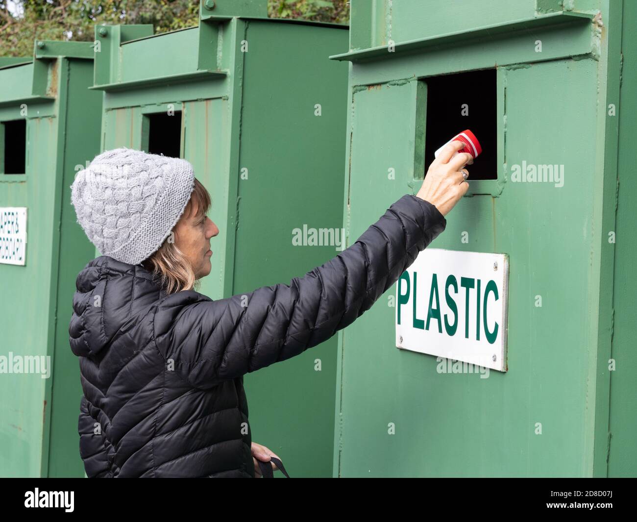 Eine Dame wird gesehen, wie sie Recycling in beschriftete grüne Behälter mit "Plastik" legt. Stockfoto