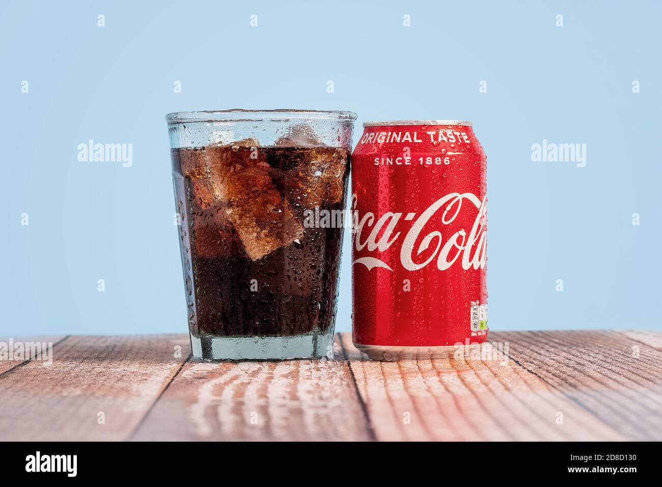 London, Vereinigtes Königreich - Oktober 29 2020: Eiskalte Dose von Coke sitzt neben einem vollen Glas Coca Cola auf einem Holztisch mit blauem Hintergrund Stockfoto