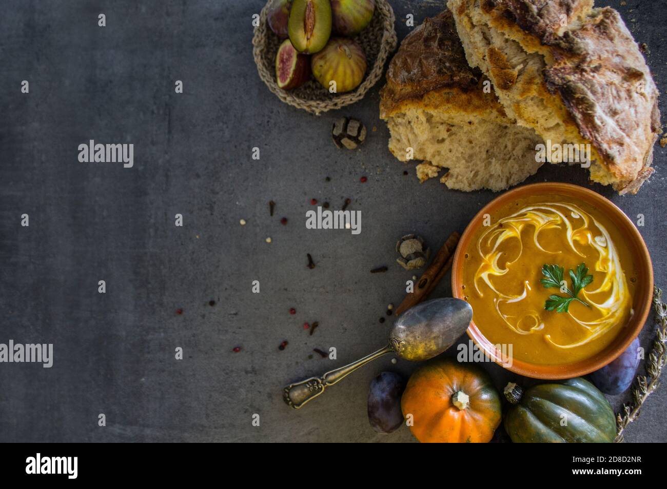 Kürbissuppe mit frisch gebackenem Brot und silbernem Löffel auf grauem Tisch. Foto der veganen Mahlzeit von oben. Gesunde Ernährung Konzept. Stockfoto