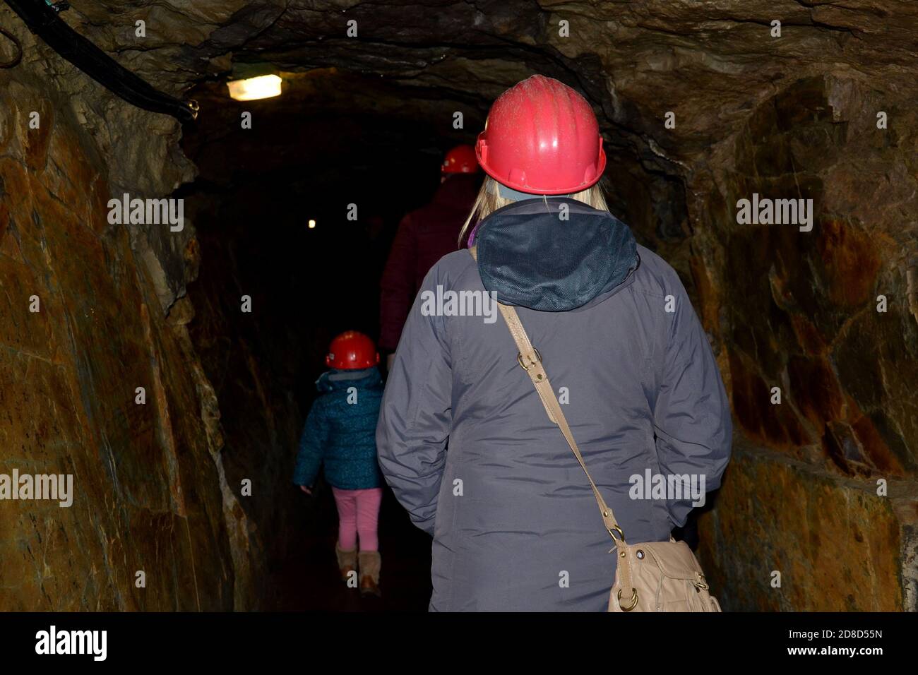 Nahaufnahme einer Frau mit rotem Schutzhelm und grauer Jacke und einem kleinen Kind mit Helm in der Ferne, in einer dunklen Höhle Stockfoto