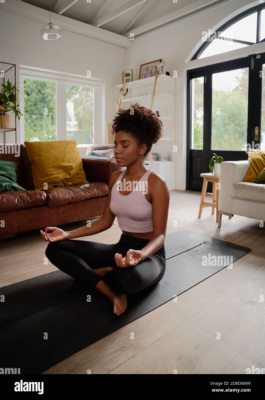 Afrikanische junge Frau in Lotusposition, die Meditation und Atmung praktiziert Sport zu Hause Stockfoto