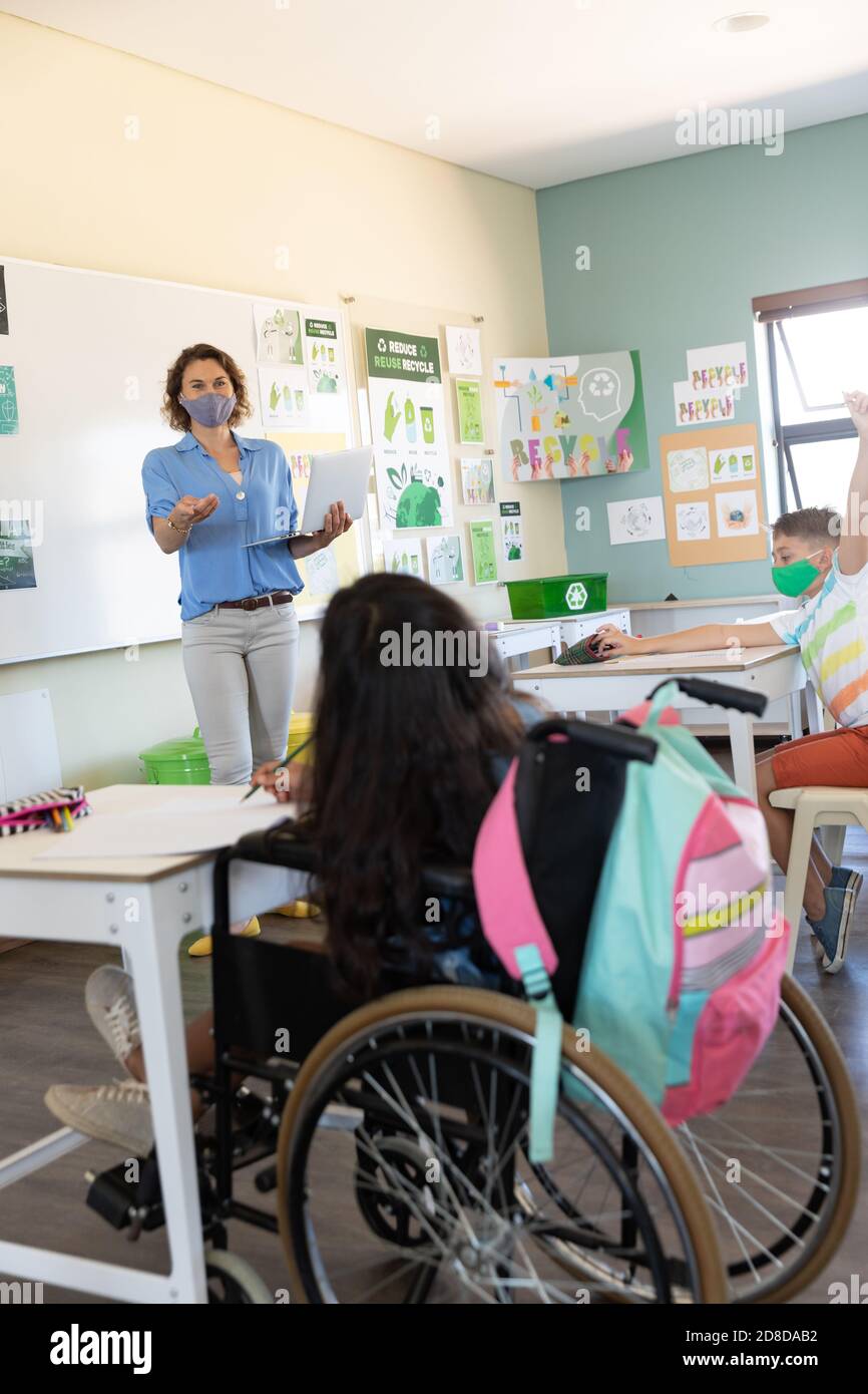 Weibliche Lehrerin trägt Gesichtsmaske mit Laptop, um Schüler zu lehren In der Klasse Stockfoto