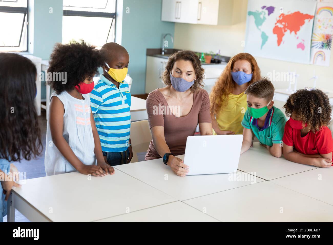 Weibliche Lehrerin trägt Gesichtsmaske mit Laptop, um Schüler zu lehren In der Klasse Stockfoto