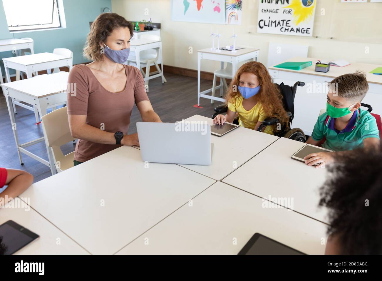 Weibliche Lehrerin trägt Gesichtsmaske mit Laptop, um Schüler zu lehren In der Klasse Stockfoto