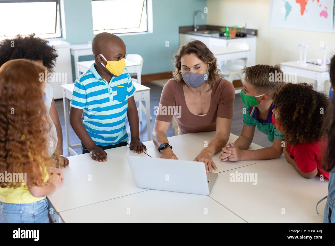 Weibliche Lehrerin trägt Gesichtsmaske mit Laptop, um Schüler zu lehren In der Klasse Stockfoto