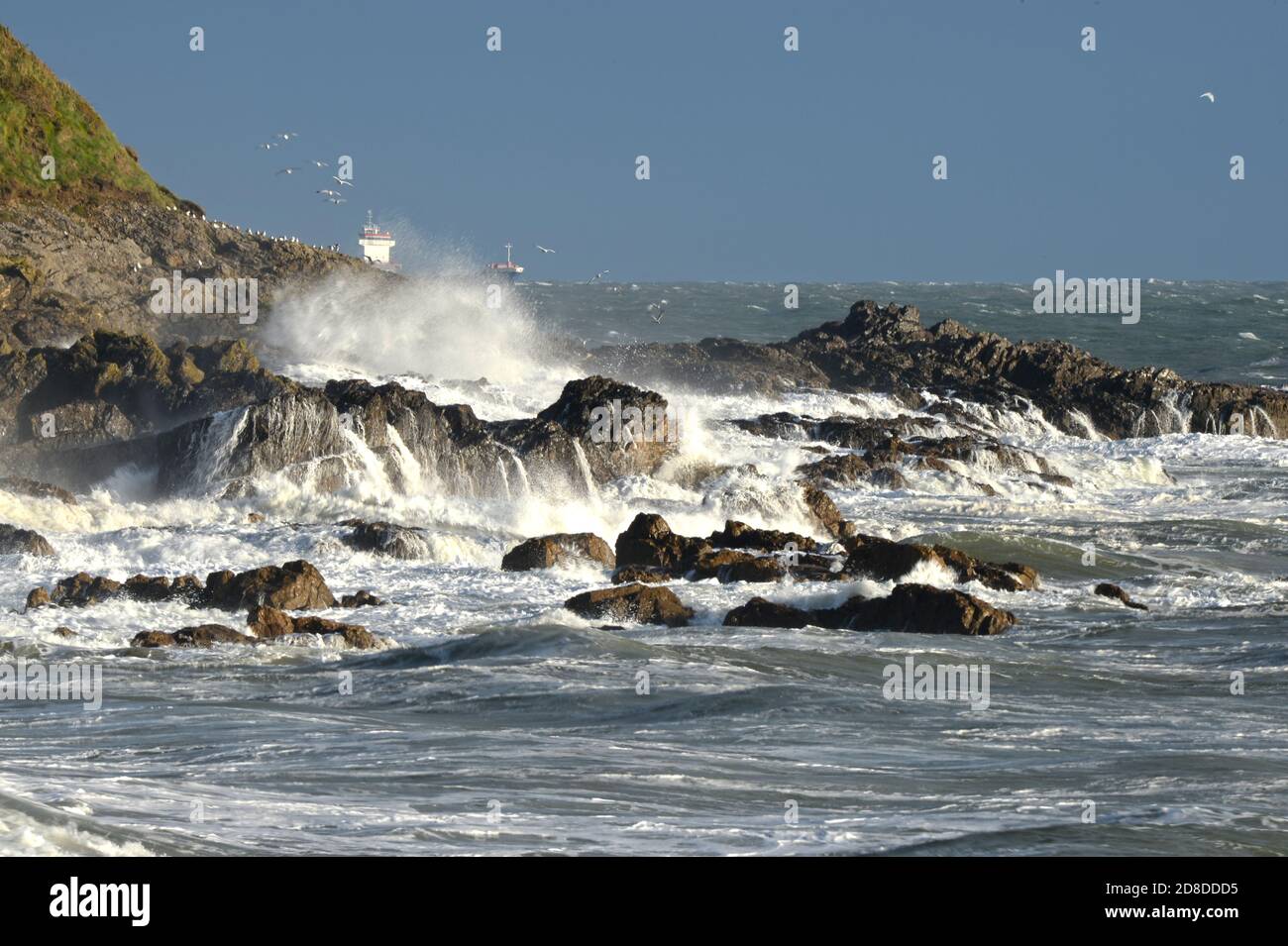 Große Welle überflutet die Felsen auf dieser Landzunge auf Gower und sendet Ströme von Wasser auf das Land. Ein Schiff reitet im Hintergrund den Sturm Stockfoto