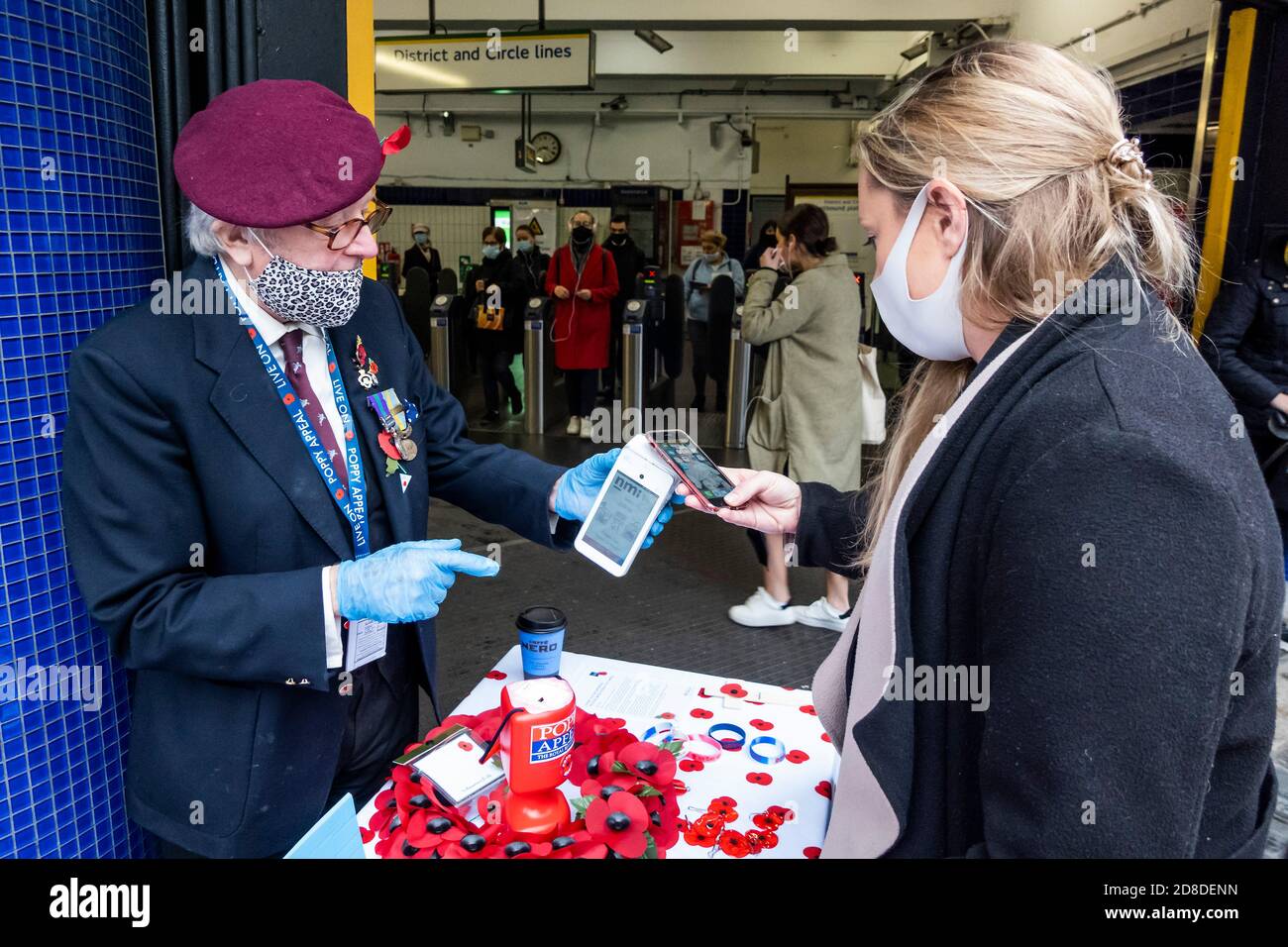 London, Großbritannien. Okt. 2020. Es ist der London Poppy Day und ein Veteran (in der Gruppe der Risikogruppen) der Luftlandetruppen, in seiner roten Baskenmütze, sammelt sich für die Royal British Legion, als ein stetiger Passagierstrom die U-Bahnstation Sloane Square verlässt. Er trägt eine Maske und Handschuhe und sammelt meist Geld mit kontaktlosen Zahlungen (obwohl er immer noch eine "Dose" für Bargeld hat). Reisende tragen meist Masken, nachdem sie obligatorisch geworden sind. Kredit: Guy Bell/Alamy Live Nachrichten Stockfoto
