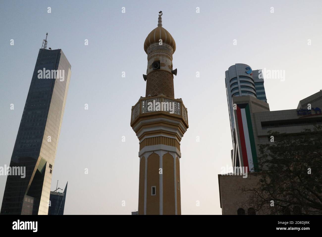 Minarett der Moschee zwischen Hochhäusern mit Kuwait Flagge Stockfoto