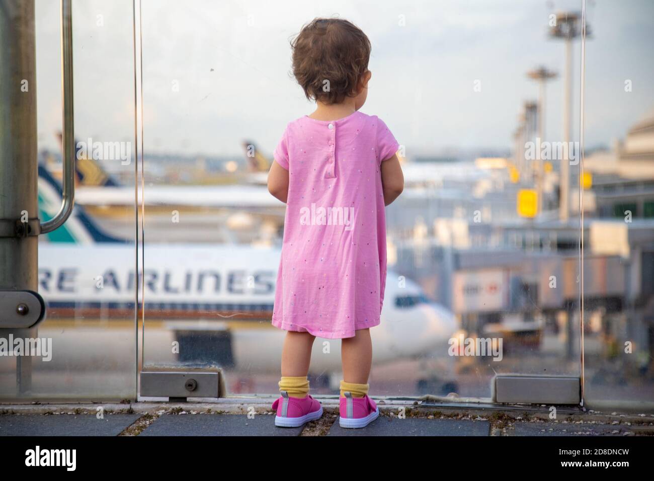SINGAPUR - FEBRUAR 11 2020: Kleinkind in Pink Dress sieht sich Singapore Airlines geparkte Flugzeuge am Changi Airport an Stockfoto