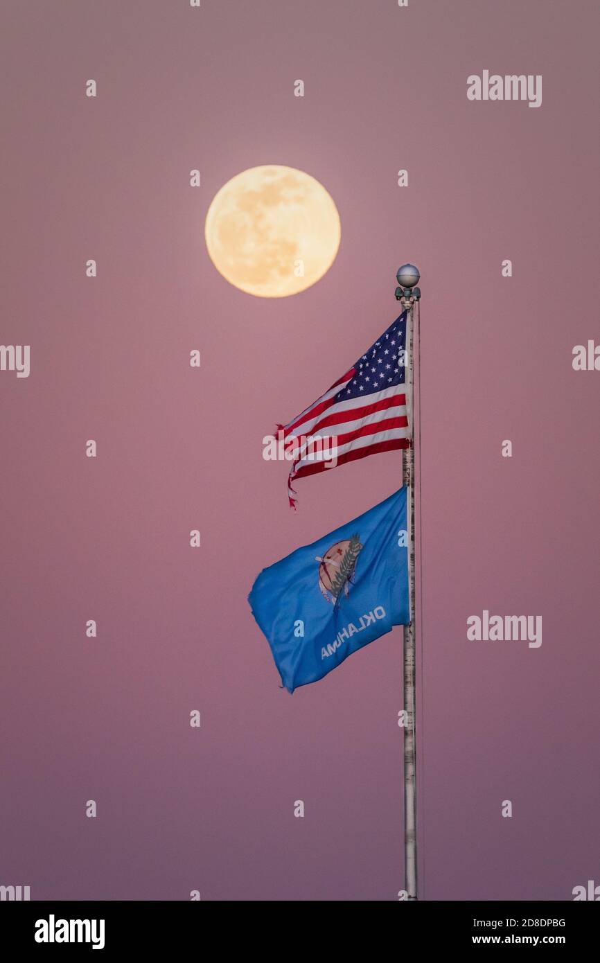 Ein schöner Vollmond, der über die amerikanische und Oklahoma Flag steigt, während die Sonne untergeht. Stockfoto