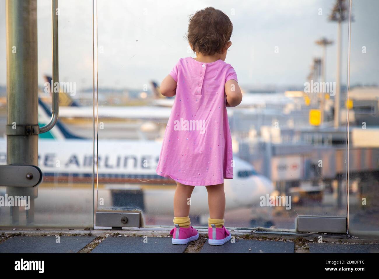 SINGAPUR - FEBRUAR 11 2020: Kleinkind in Pink Dress sieht sich Singapore Airlines geparkte Flugzeuge am Changi Airport an Stockfoto