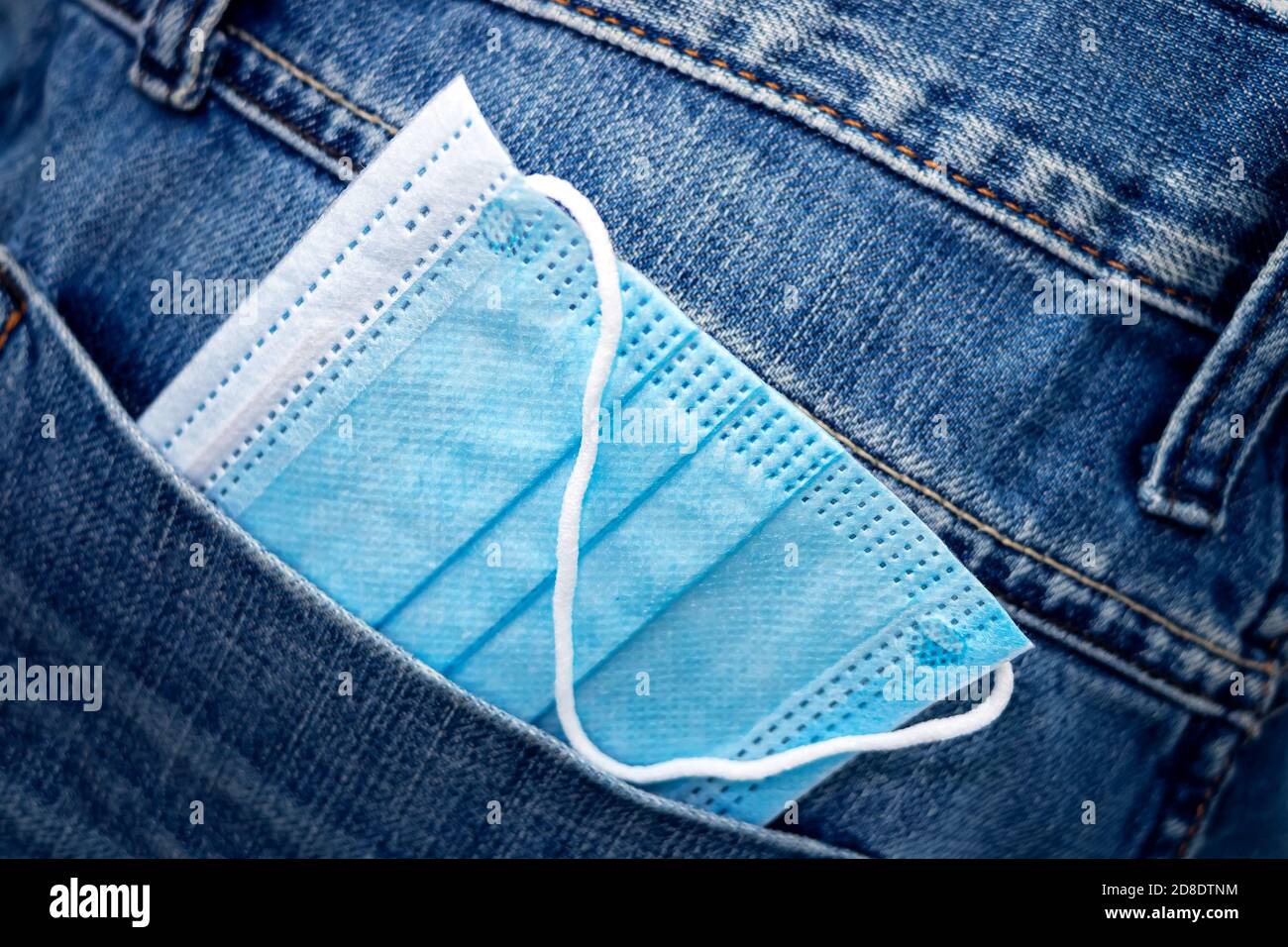 Medizinische Maske in der Gesäßtasche der Jeans. Blaue medizinische Maske in einer Denim-Tasche. Nahaufnahme Stockfoto