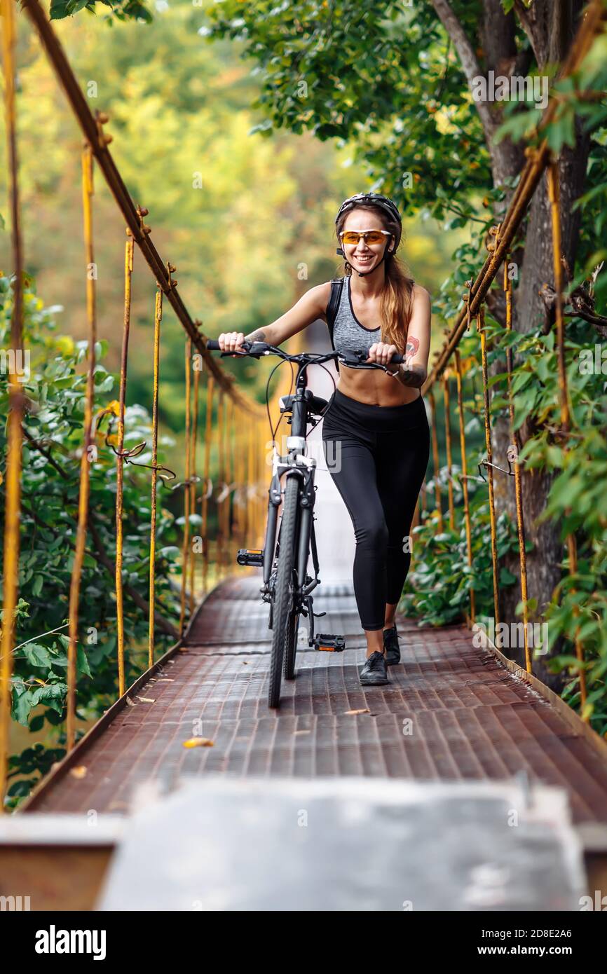 Attraktive Passform junge Frau trägt Sportbekleidung mit ihrem Fahrrad auf Hängebrücke im Herbst Stockfoto