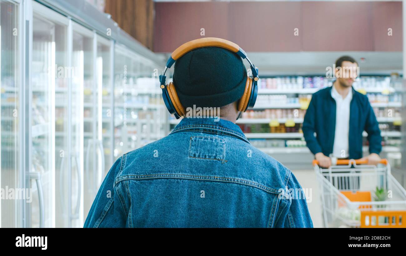 Im Supermarkt: Stilvoller African American Guy mit Kopfhörern geht durch die Frozen Goods Section des Stores. Nach Der Rückansicht. Stockfoto