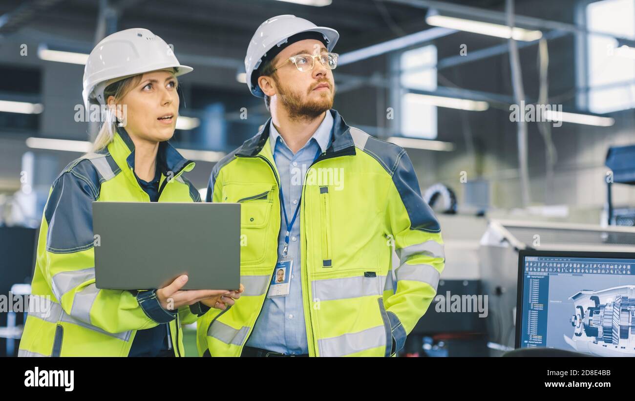 In der Fertigungsfabrik arbeitet ein männlicher Mechaniker am Personal Computer unter der Aufsicht eines weiblichen Projektingenieurs. Stockfoto