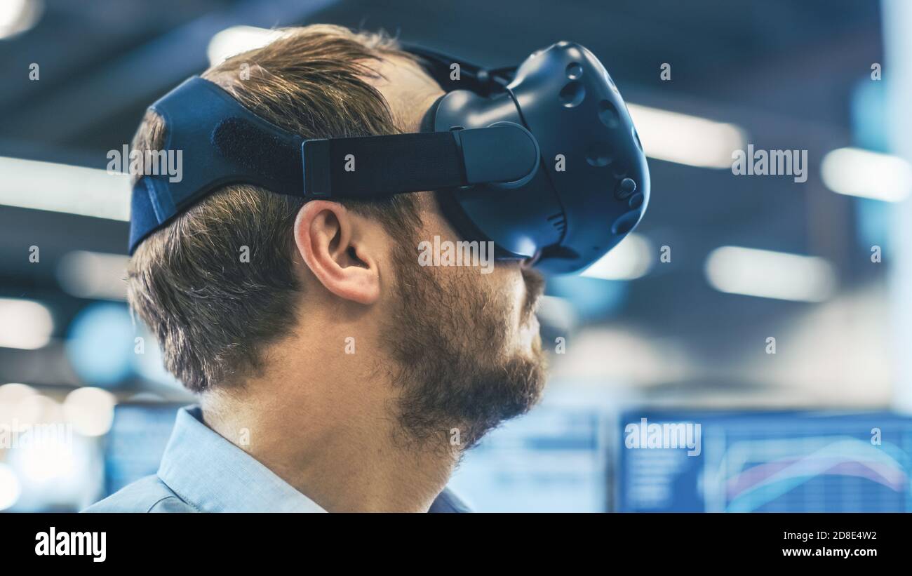 Portraitaufnahme des Industrieingenieurs mit Virtual Reality Headset und Gestik mit Controllern. Im Hintergrund werden „nicht fokussiert“ und angezeigt Stockfoto