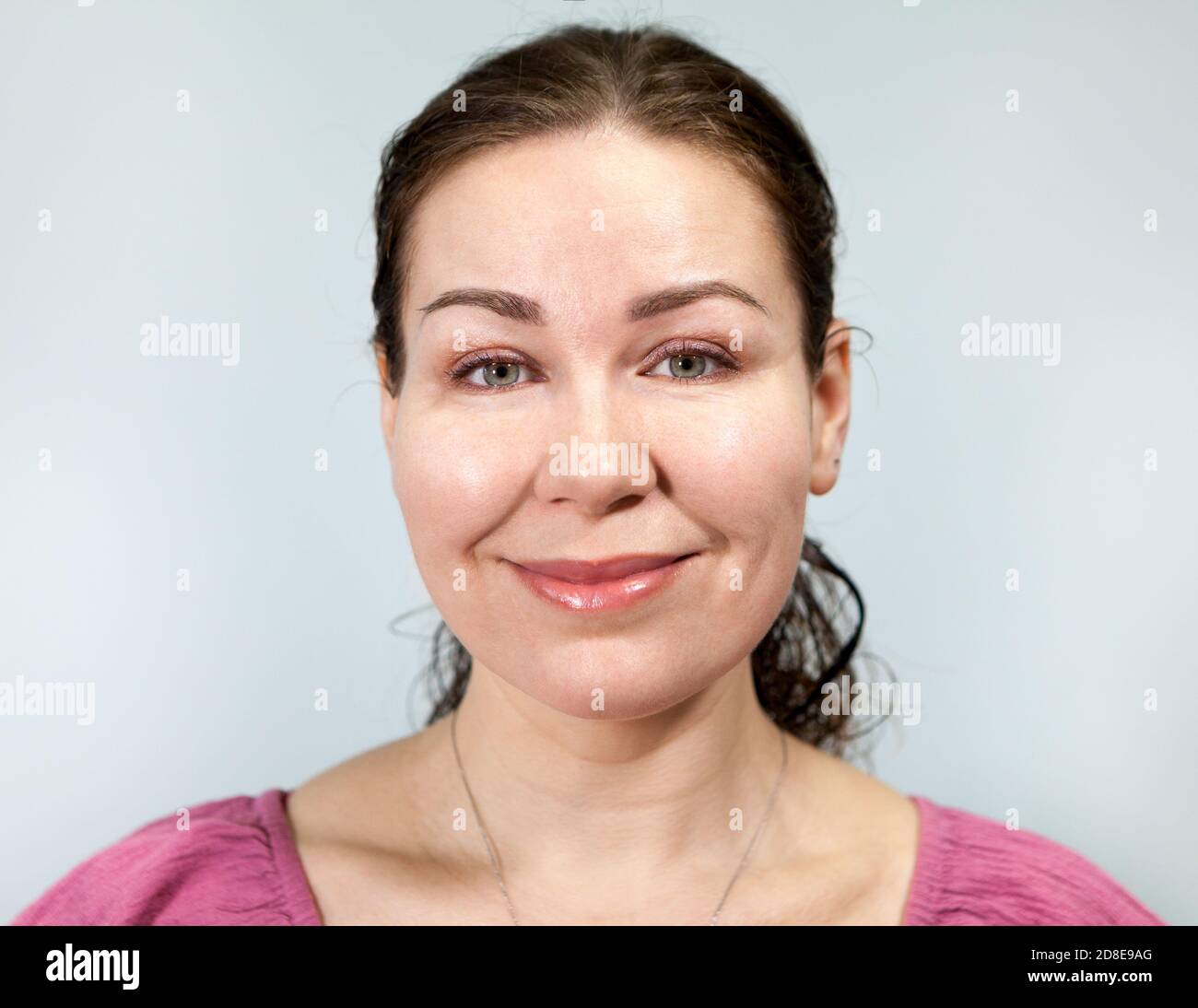 Lächelnd gutmütige kaukasische Erwachsene Frau, Porträt auf grauem Hintergrund, Emotionen-Serie Stockfoto